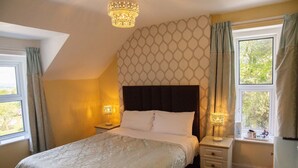 Une chambre avec un grand lit, deux tables de chevet avec des lampes, une fenêtre avec des rideaux et un mur décoré d’un motif.