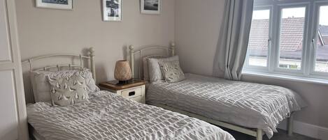 A bedroom with two single beds, a nightstand, a lamp, and a window with curtains.