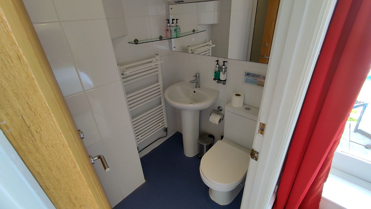A small bathroom with a white sink, toilet, and a mirror above the sink. There are toiletries on the wall and a towel rack.