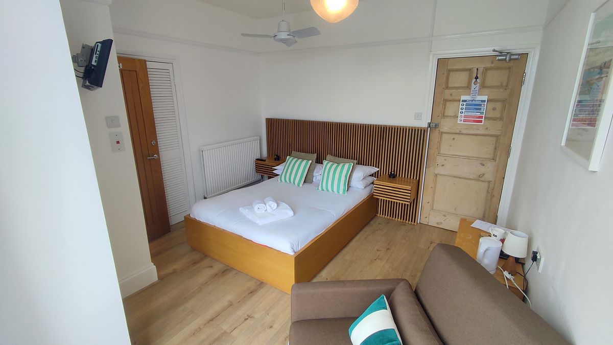 Een slaapkamer met een houten bed, een houten hoofdbord, een nachtkastje met een lamp en een deur met een veiligheidsbordje.
