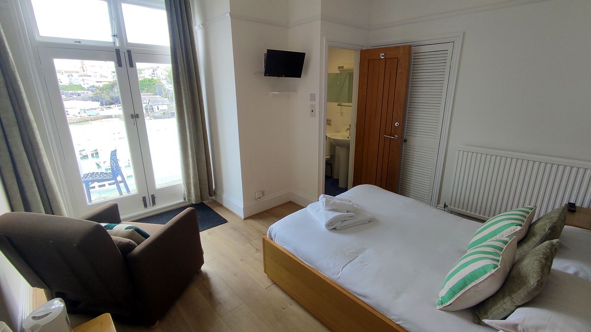 A hotel room with a bed, a chair, a TV, and a view of the outside.