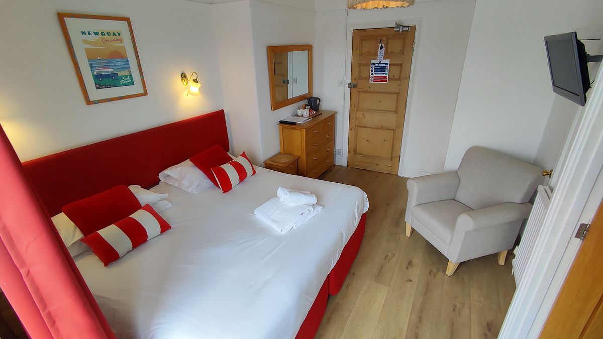 A hotel room with a bed, a chair, a dresser, a mirror, a television, and a door with a sign.
