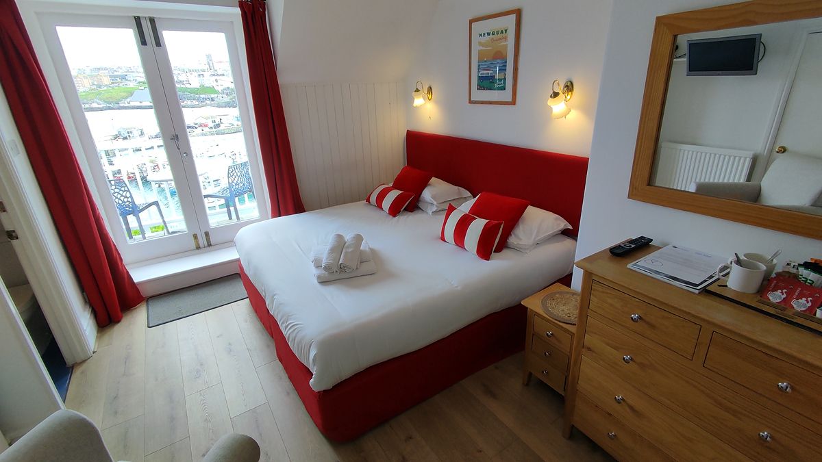 A hotel room with a bed, a wooden dresser, a mirror, a window with curtains, and a view of the outside.