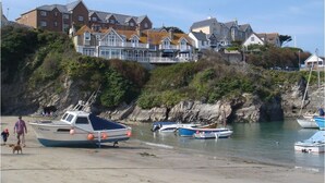 Une ville côtière avec des maisons construites sur une colline, des bateaux sur la plage et une personne promenant un chien.
