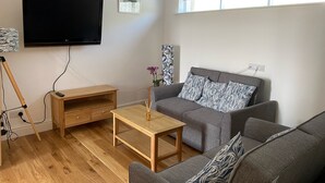 Un salon moderne avec un canapé gris, une table basse en bois, un téléviseur fixé au mur et une fenêtre agrémentée de rideaux à motifs.