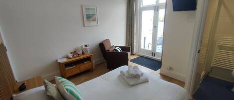 A hotel room with a bed, a chair, a small table with a lamp, a picture on the wall, and a window with curtains.