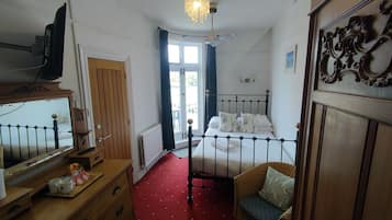 A bedroom with a bed, a chair, a desk, a mirror, a radiator, and a window with curtains.