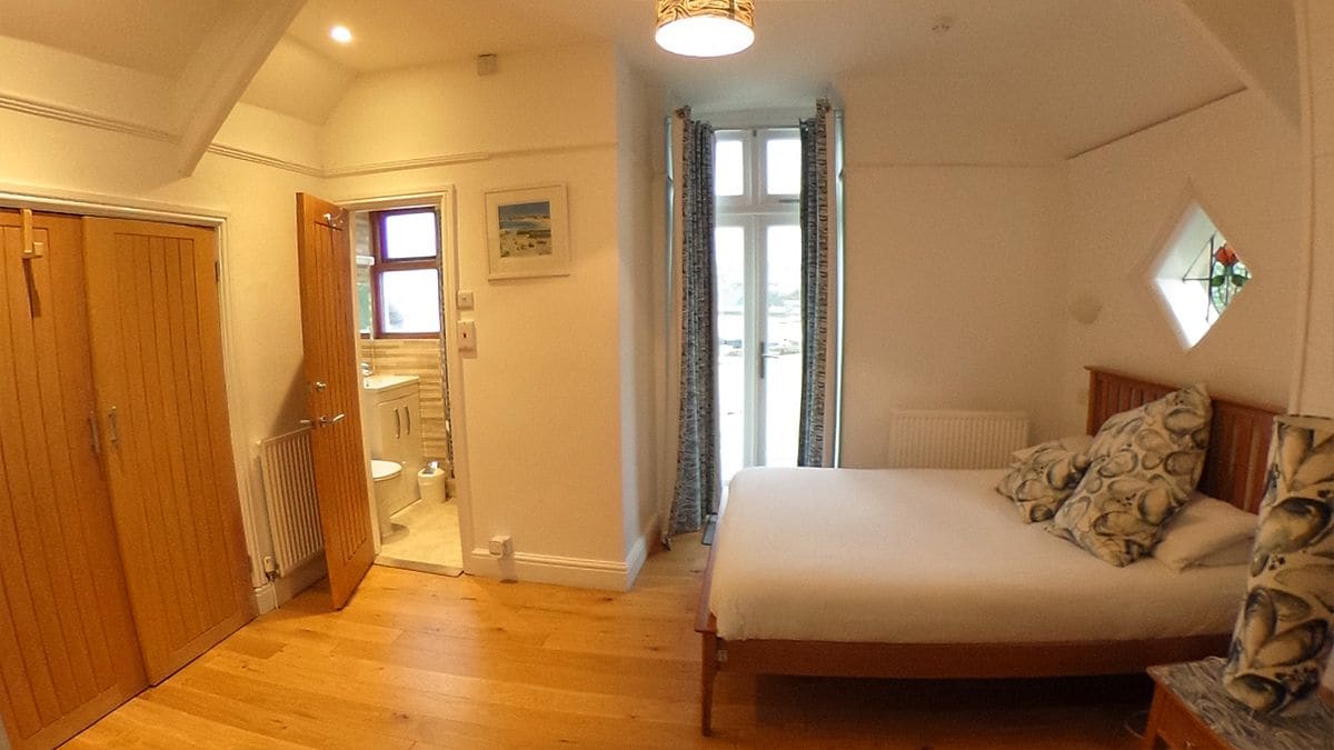 Un dormitorio con cama, ventana con cortinas, radiador y puerta de madera.
