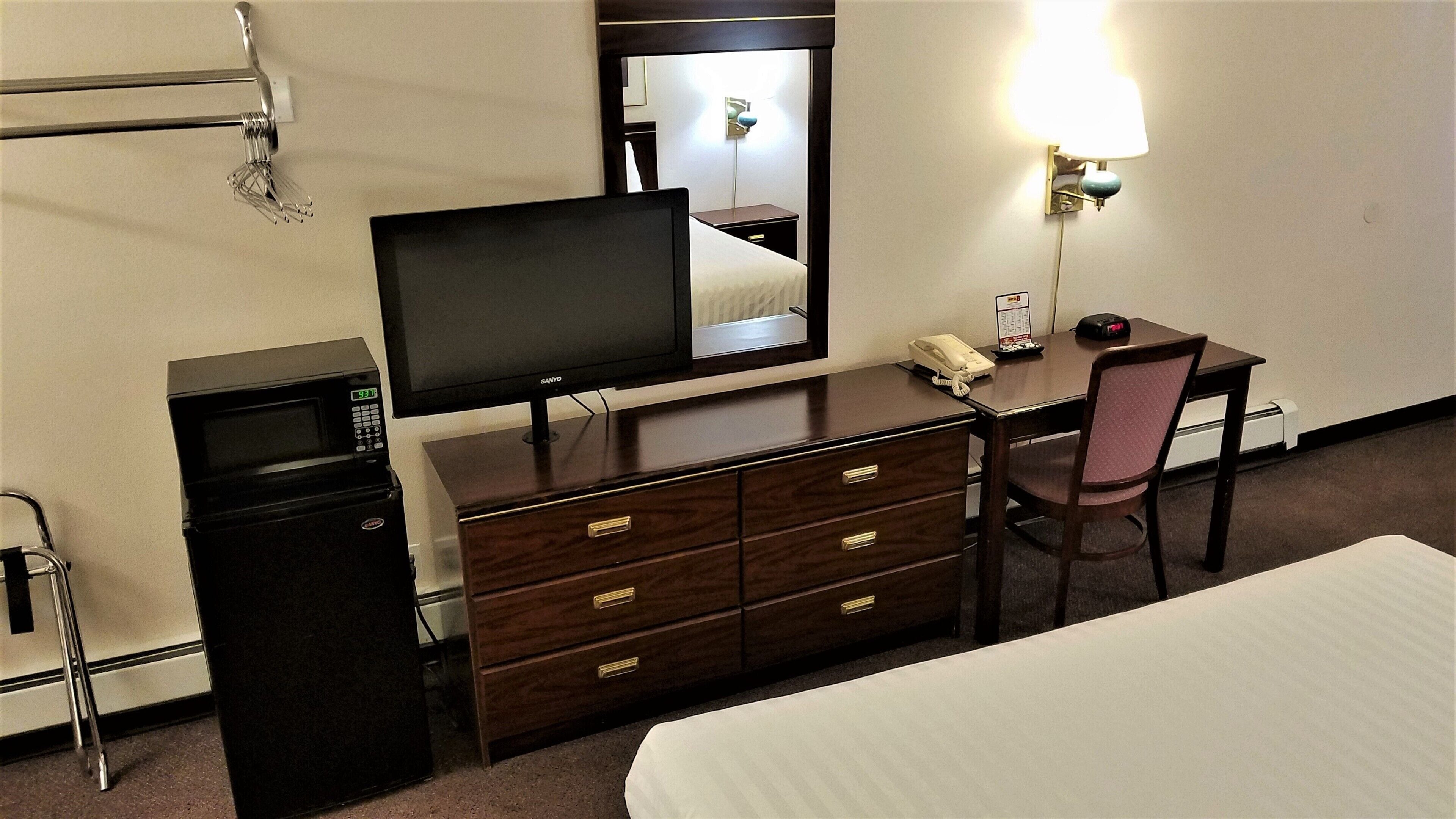 A hotel room with a bed, a desk with a chair, a television, a microwave, and a telephone.