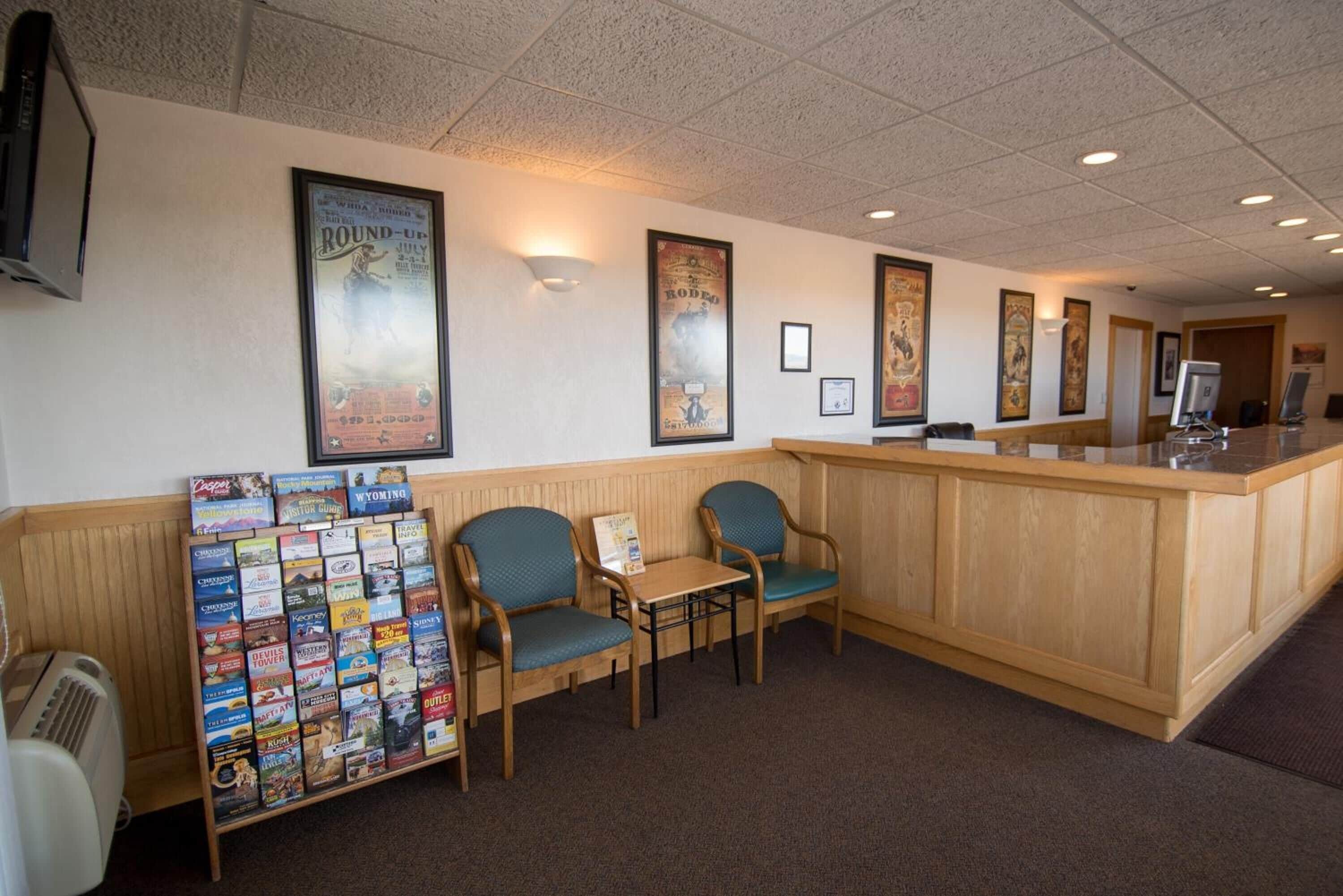 A reception area with a wooden counter, two blue chairs, a small table, and a wall display of brochures.