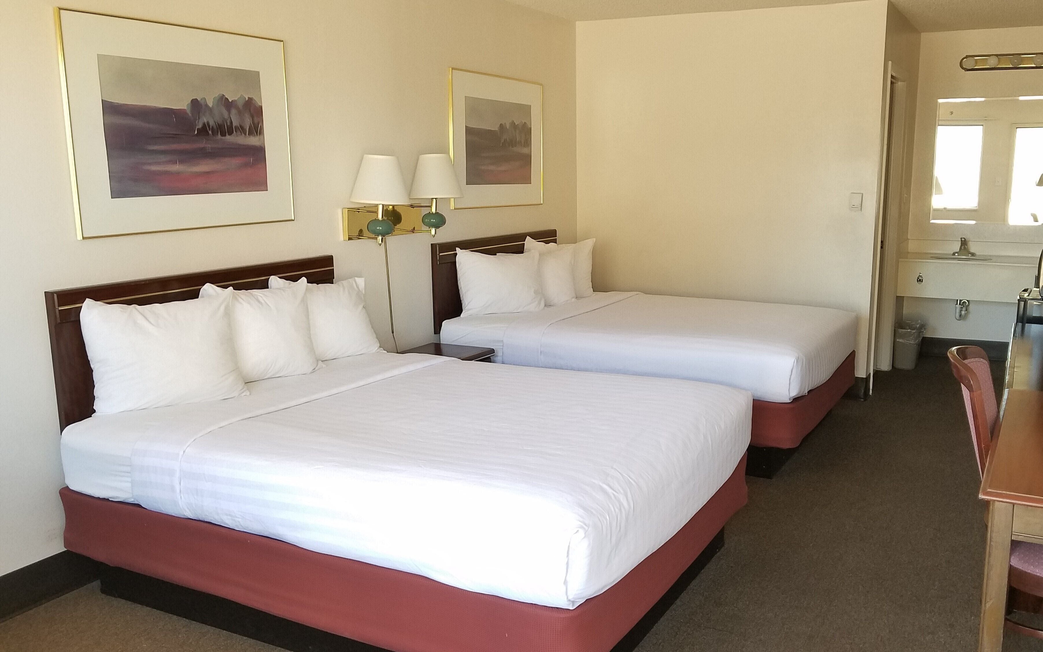 Habitación de hotel con dos camas, una mesita de noche, una lámpara y dos cuadros en la pared.