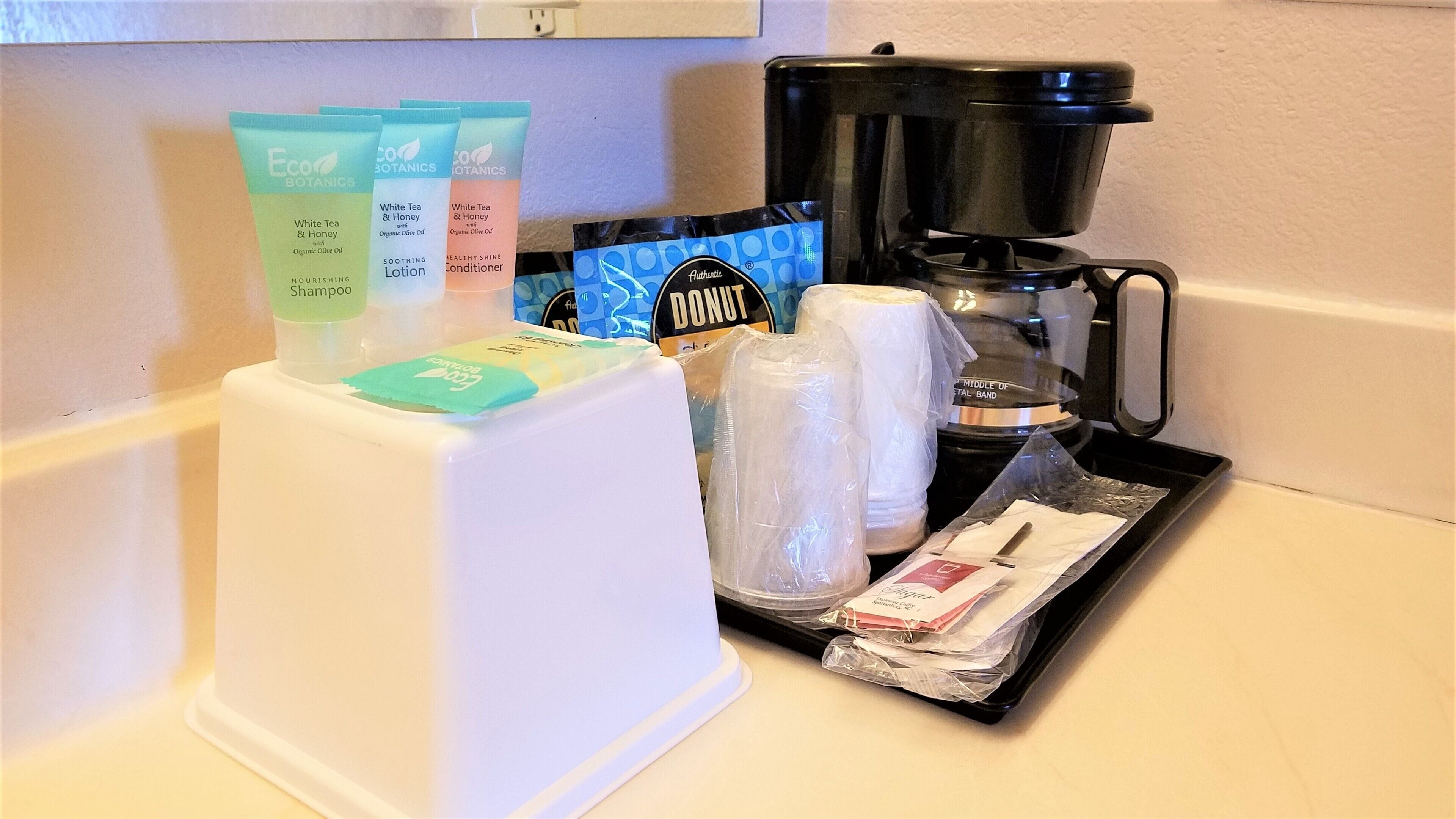 A kitchen counter with toiletries, a coffee maker, and a trash bin.