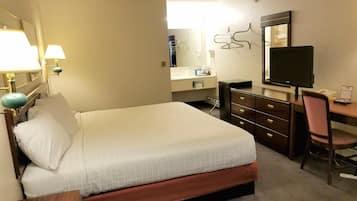 A hotel room with a bed, a desk with a computer, a chair, a dresser, a mirror, and a lamp.