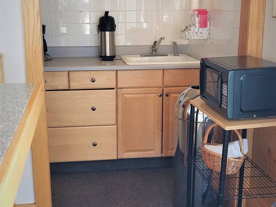 A compact kitchen with wooden cabinets, a microwave, a kettle, and a sink.