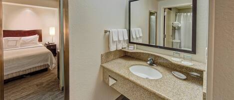 A hotel room with a bed, a bathroom with a sink, mirror, and towels.