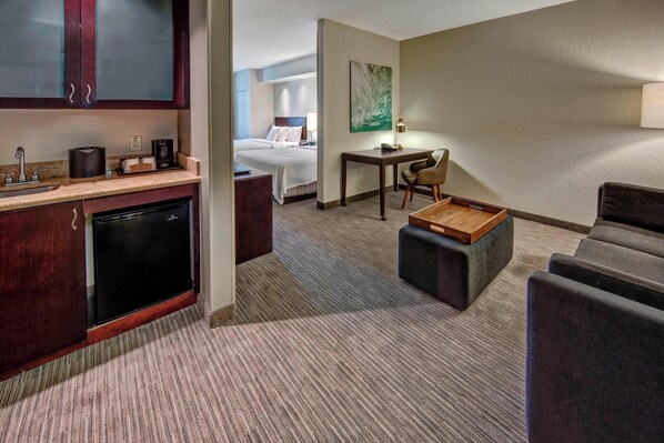 A hotel room with a kitchenette, a bed, a desk, and a seating area.