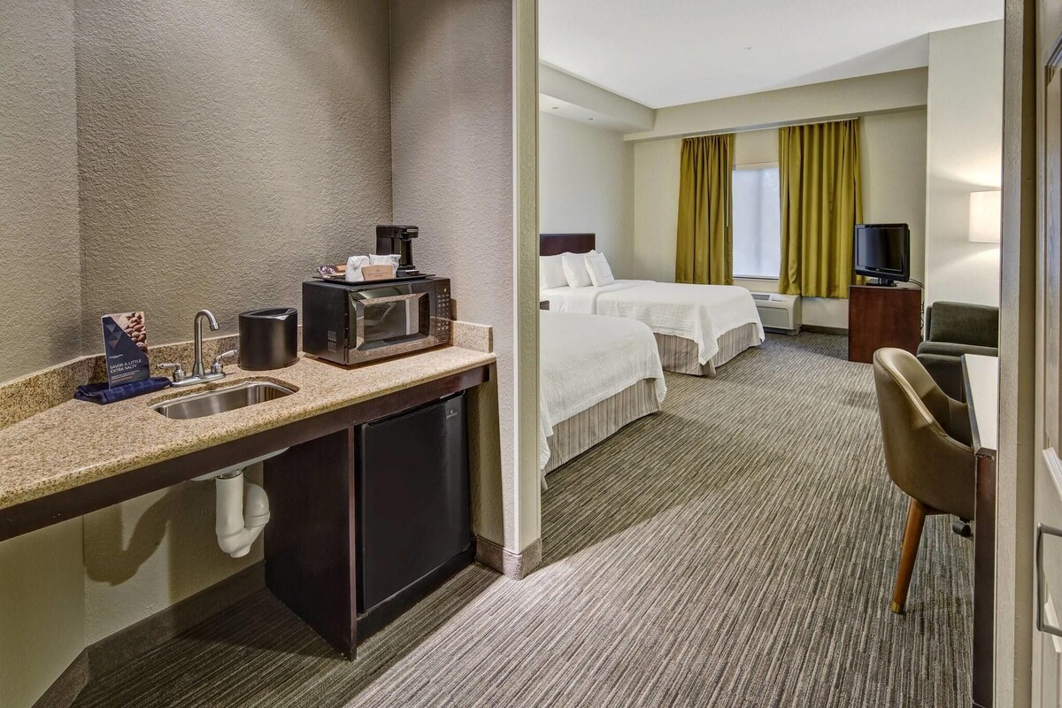 A hotel room with a kitchenette, a bed, a TV, and a seating area.
