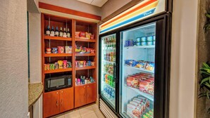 Una kitchenette con microondas, repisas llenas de bocadillos y un refrigerador que contiene bebidas y alimentos.