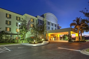 A hotel entrance with a covered driveway, a parking lot, and a building with multiple floors and windows. - Springhill Suites Naples (Naples)