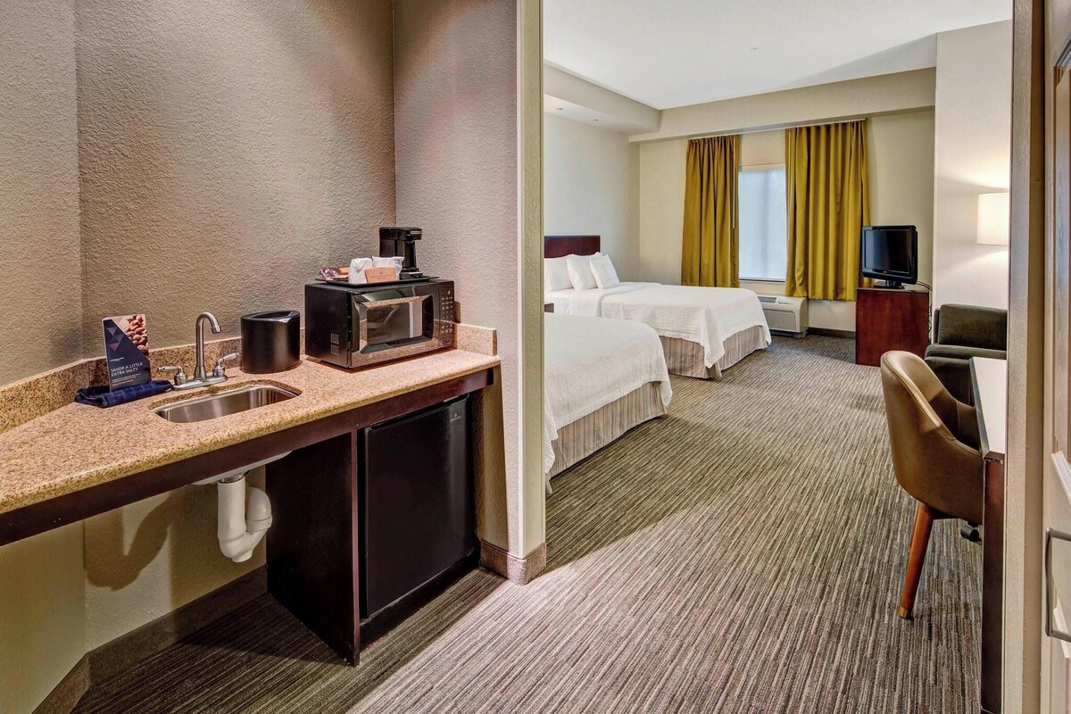 A hotel room with a kitchenette, a bed, a TV, and a seating area.