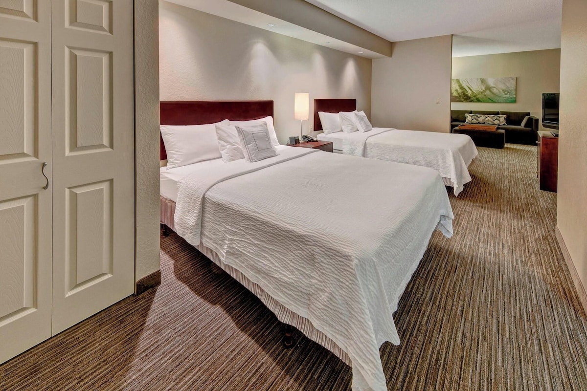 A hotel room with two beds, a sofa, a TV, and a painting on the wall.