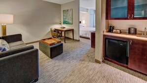 Habitación de hotel con sofá, una mesita, escritorio, kitchenette y cama.