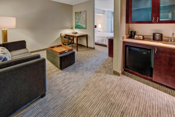 Ein Hotelzimmer mit Sofa, kleinem Tisch, Schreibtisch, Küchenzeile und Bett.