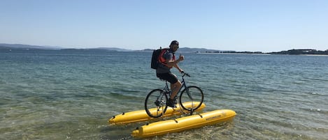 A person riding a bicycle on a yellow inflatable raft in clear water.