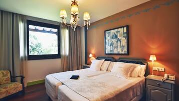 Camera d'albergo con un letto grande, un lampadario, un comodino con lampada, una sedia e una finestra con tende.