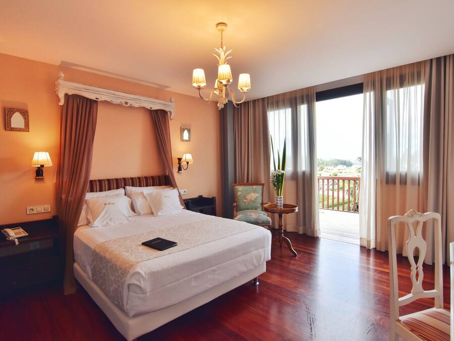 Una habitación de hotel con una cama grande, un candelabro, un balcón con vistas y una silla.
