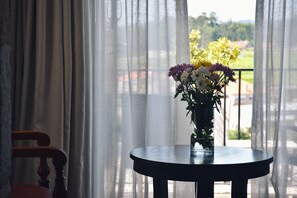Una mesa redonda con un florero frente a una ventana con cortinas traslúcidas.