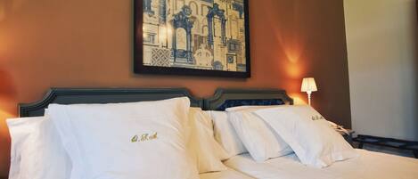 Habitación de hotel con dos camas, cada una con sábanas y almohadas blancas, un cuadro en la pared y una lámpara de noche.