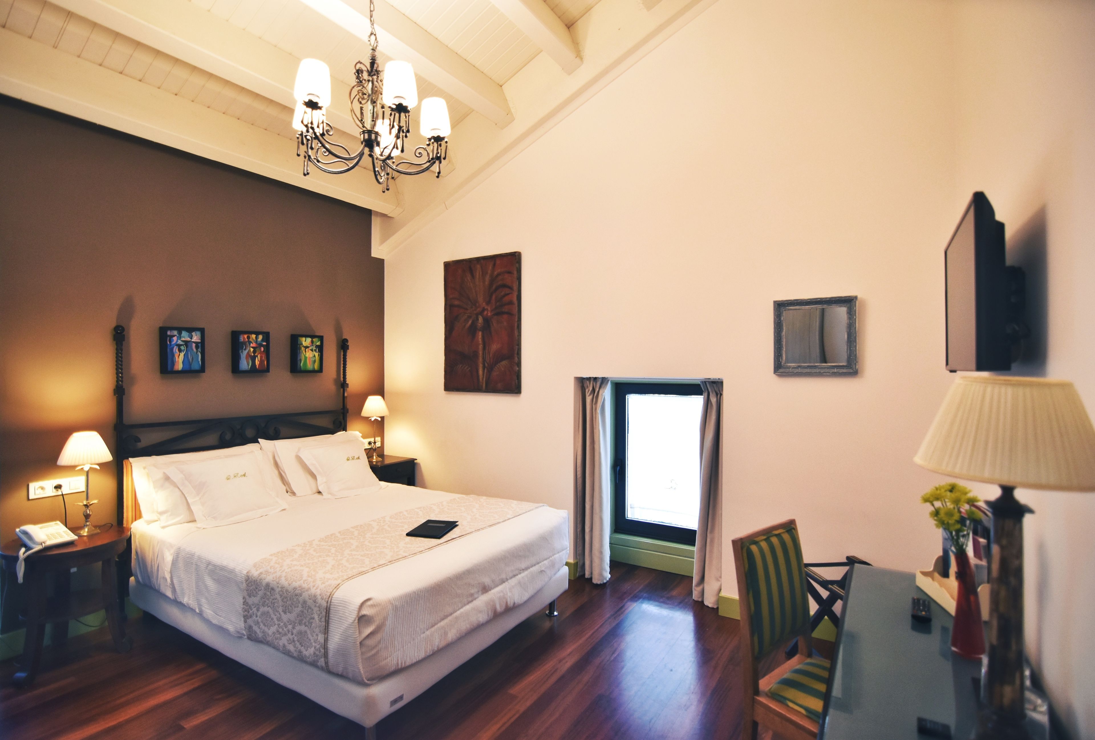 A hotel room with a large bed, bedside lamps, a desk, and a window with curtains.