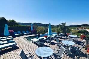 Terraza de madera con sillones, piscina y mesas con sombrillas.