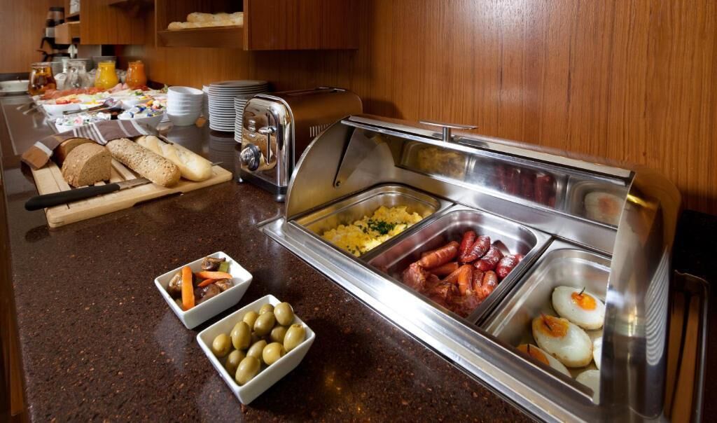 Montaje de bufé con diversos alimentos, como pan, huevos, salchichas y aceitunas.