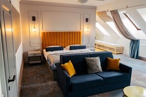 A modern bedroom with a large bed, a sofa, a bedside table, and a skylight.