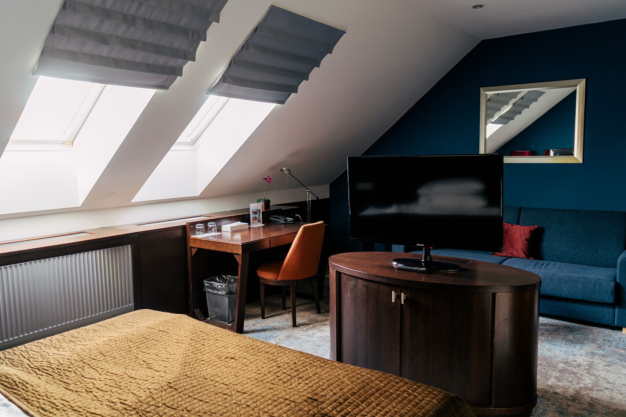 Een moderne kamer met een schuine kap, dakramen, een bureau, een bank en een televisie.