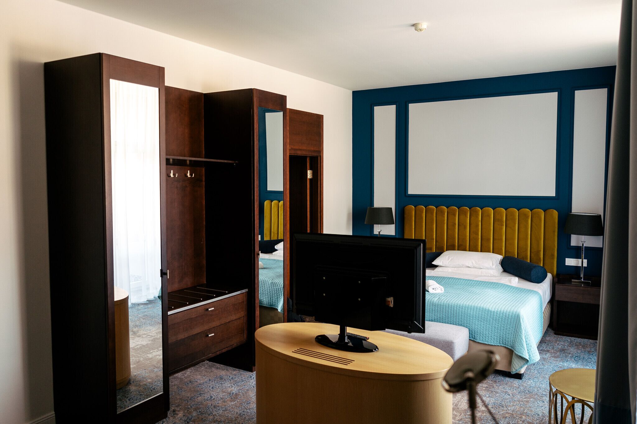 A hotel room with a bed, a desk, a chair, a wardrobe, and a television.