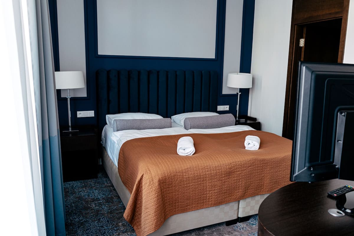 Habitación de hotel con una cama, dos lámparas de noche, un televisor y un control remoto sobre una mesita.