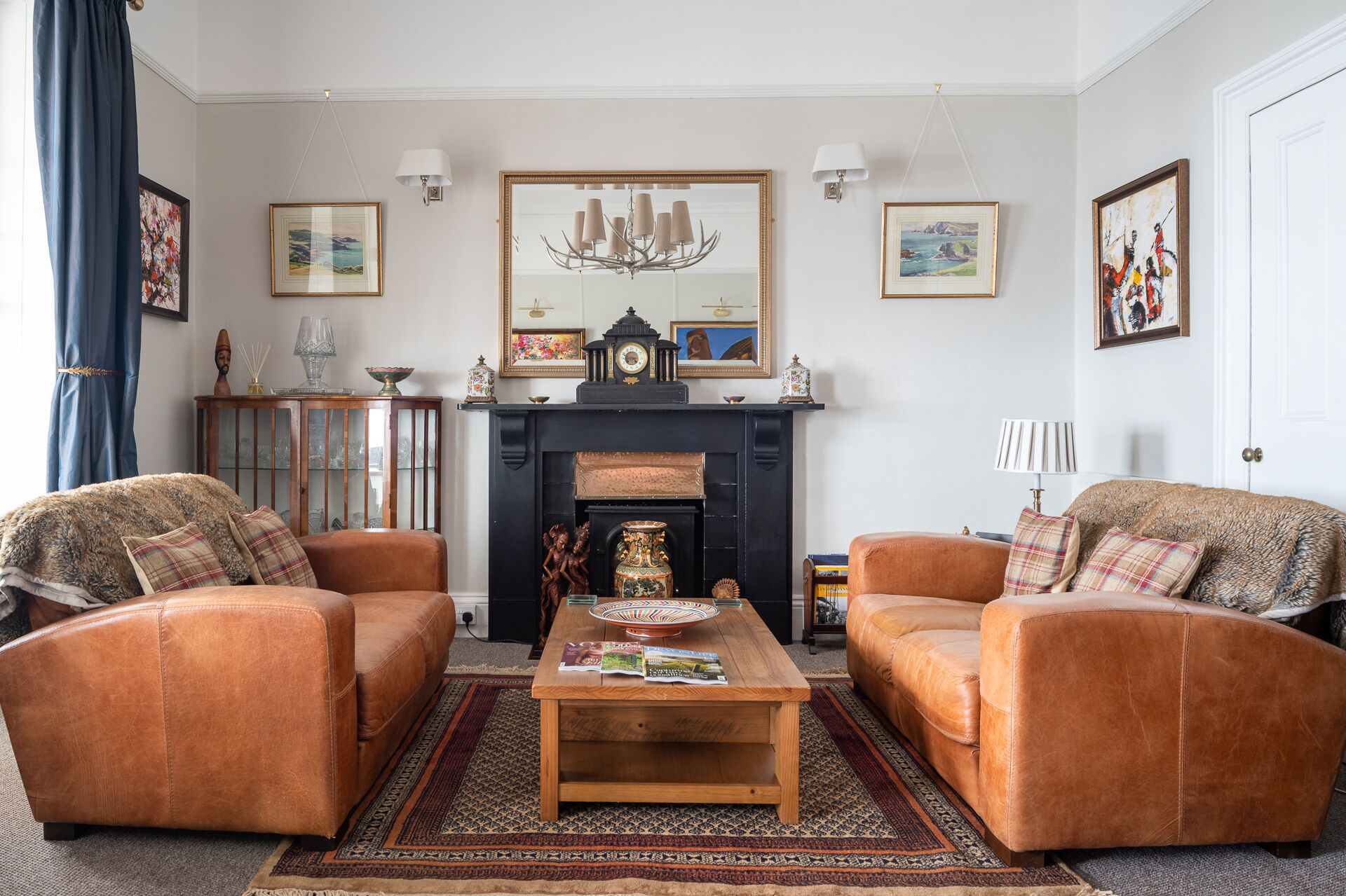A living room with two leather armchairs, a wooden coffee table, a fireplace, and various framed artworks.