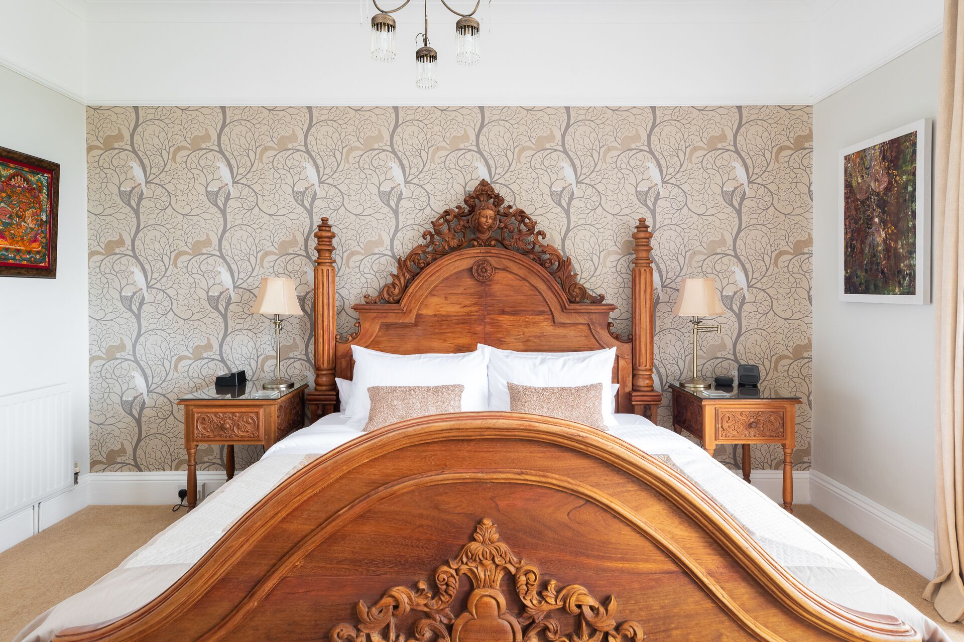 A bedroom with a large wooden bed, two bedside tables, a chandelier, and patterned wallpaper.
