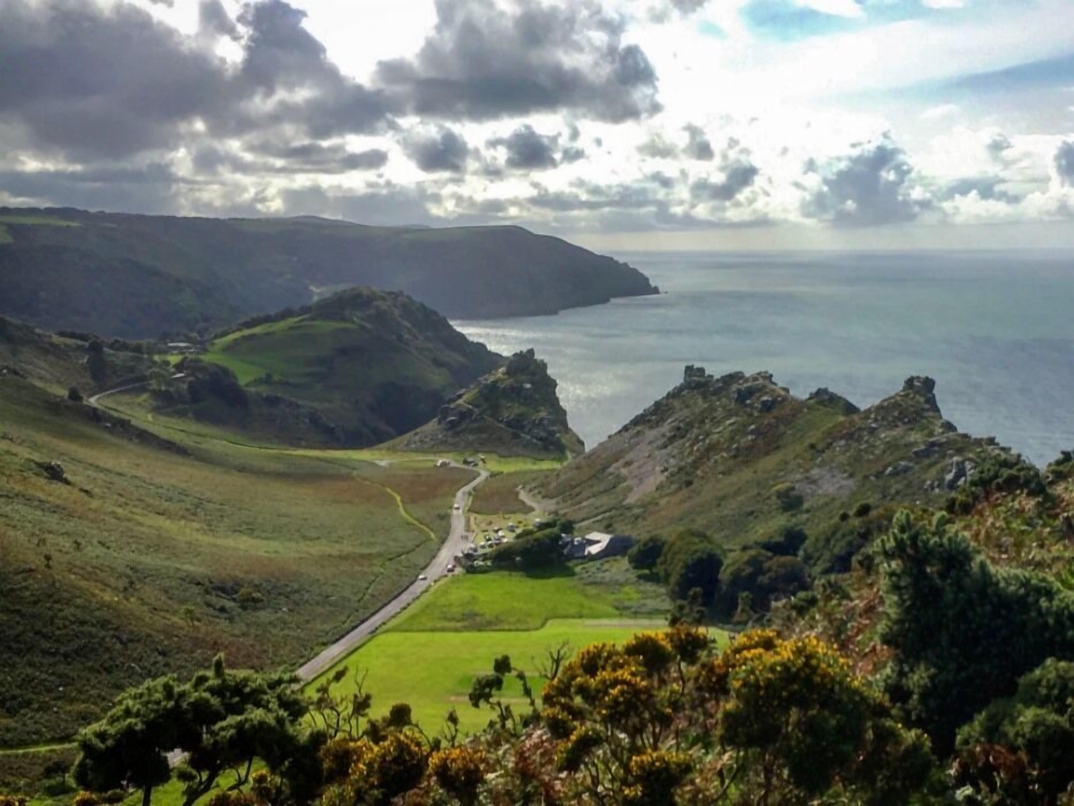 A coastal landscape with rolling hills, a winding road, and a small settlement with buildings near the shore.