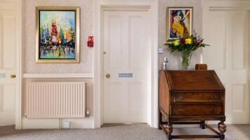 A room with a radiator, a wooden chest of drawers, and two framed paintings on the wall.