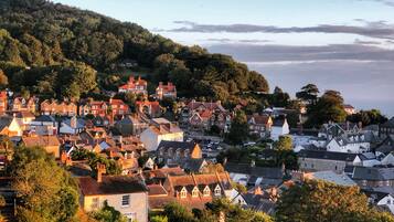 A coastal town with traditional architecture, including houses with pitched roofs and chimneys, surrounded by greenery and hills.