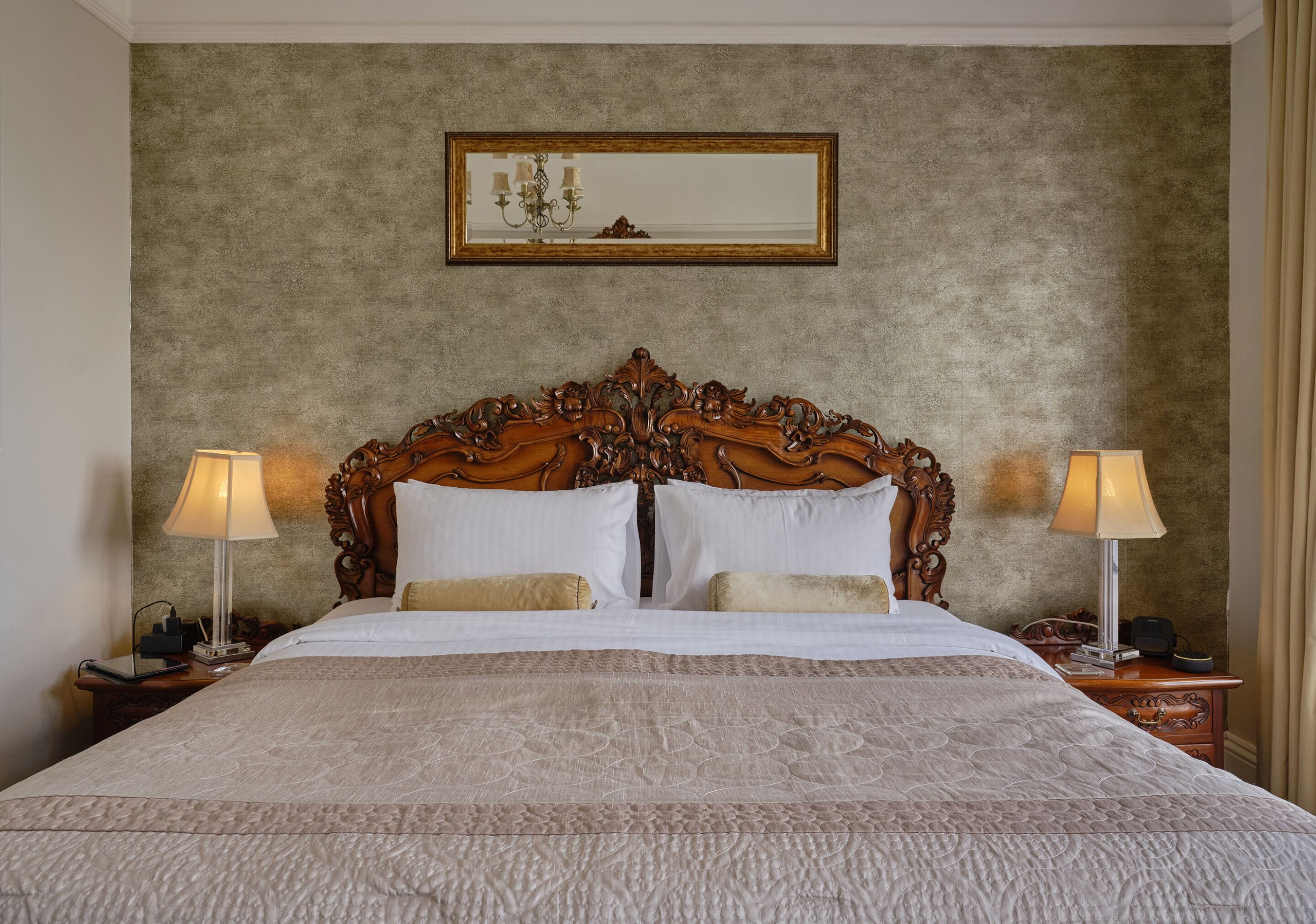 Habitación de hotel con una cama grande, un elaborada cabecera de madera, dos lámparas de noche y un cuadro enmarcado en la pared.