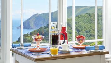 Une table de petit-déjeuner offrant une vue magnifique, avec un panier de fruits, un verre de jus d’orange et une carafe de café.