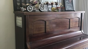 Ett pianon av trä med en dekorativ spegel ovanför, en inramad meny på väggen och en liten modellmotorcykel ovanpå.