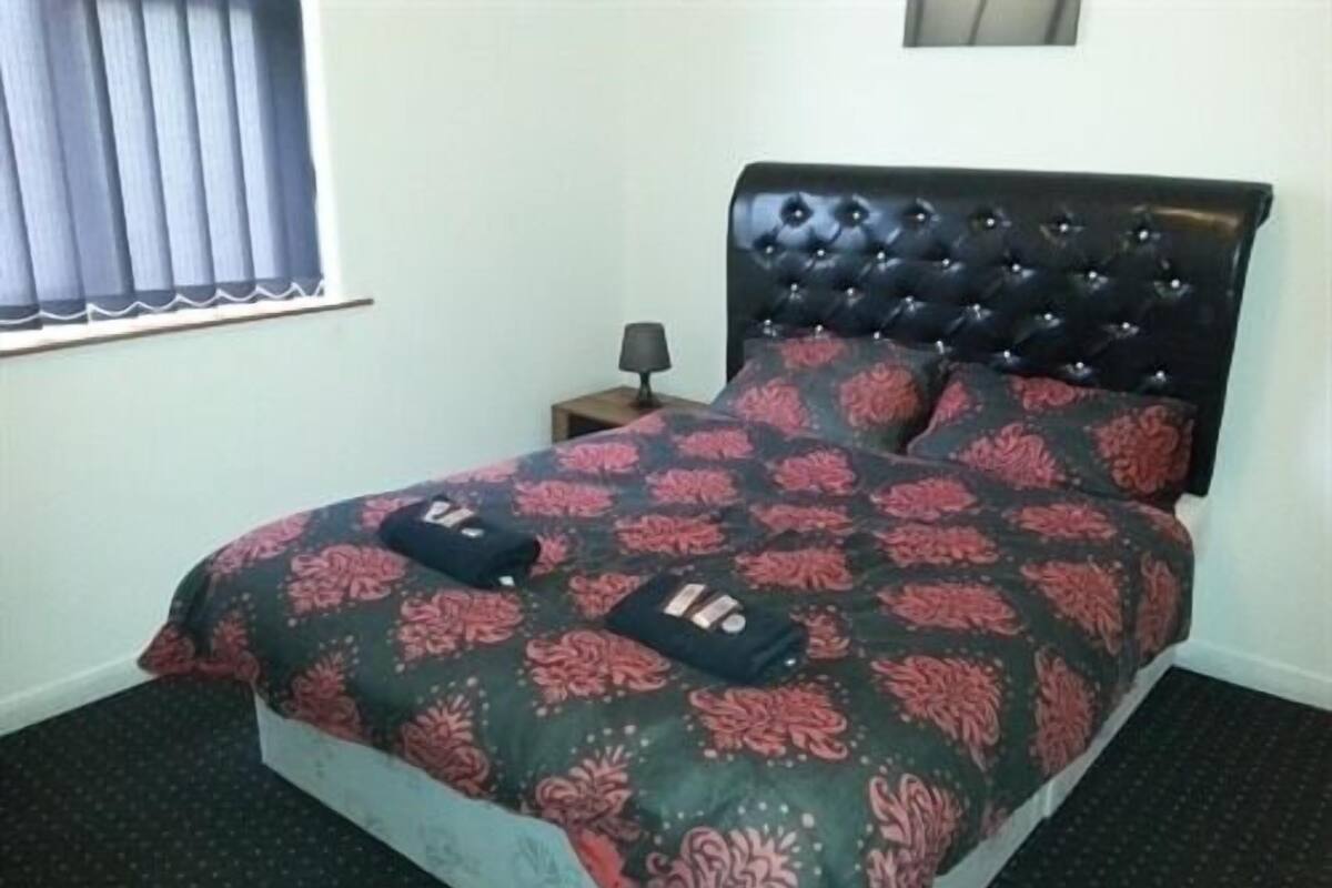 A bed with a floral bedspread, a black tufted headboard, and a small bedside table with a lamp.