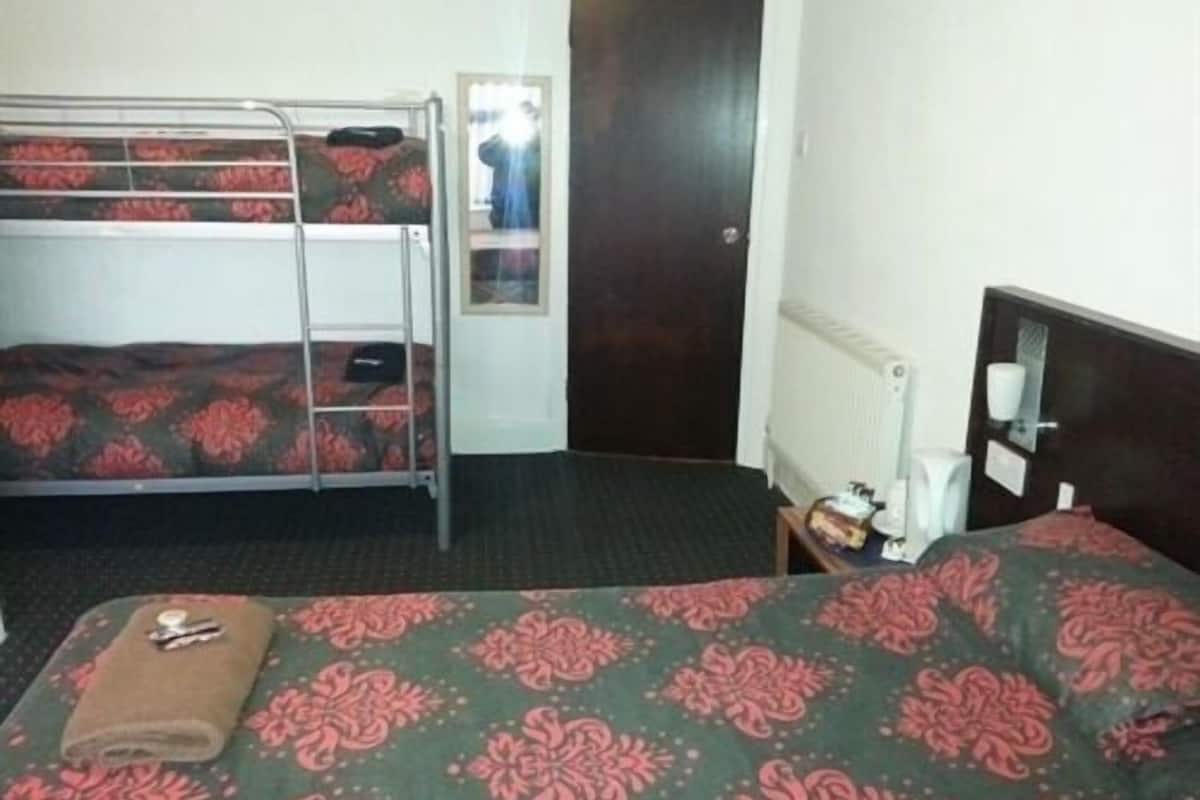 A room with a bunk bed, a single bed, a radiator, a door, and a small table with a cup and a plate.