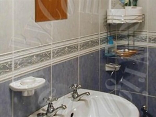 A bathroom with a white sink, a mirror, and a toilet. There are shelves with toiletries. - Twin Lions Hotel (Edinburgh)